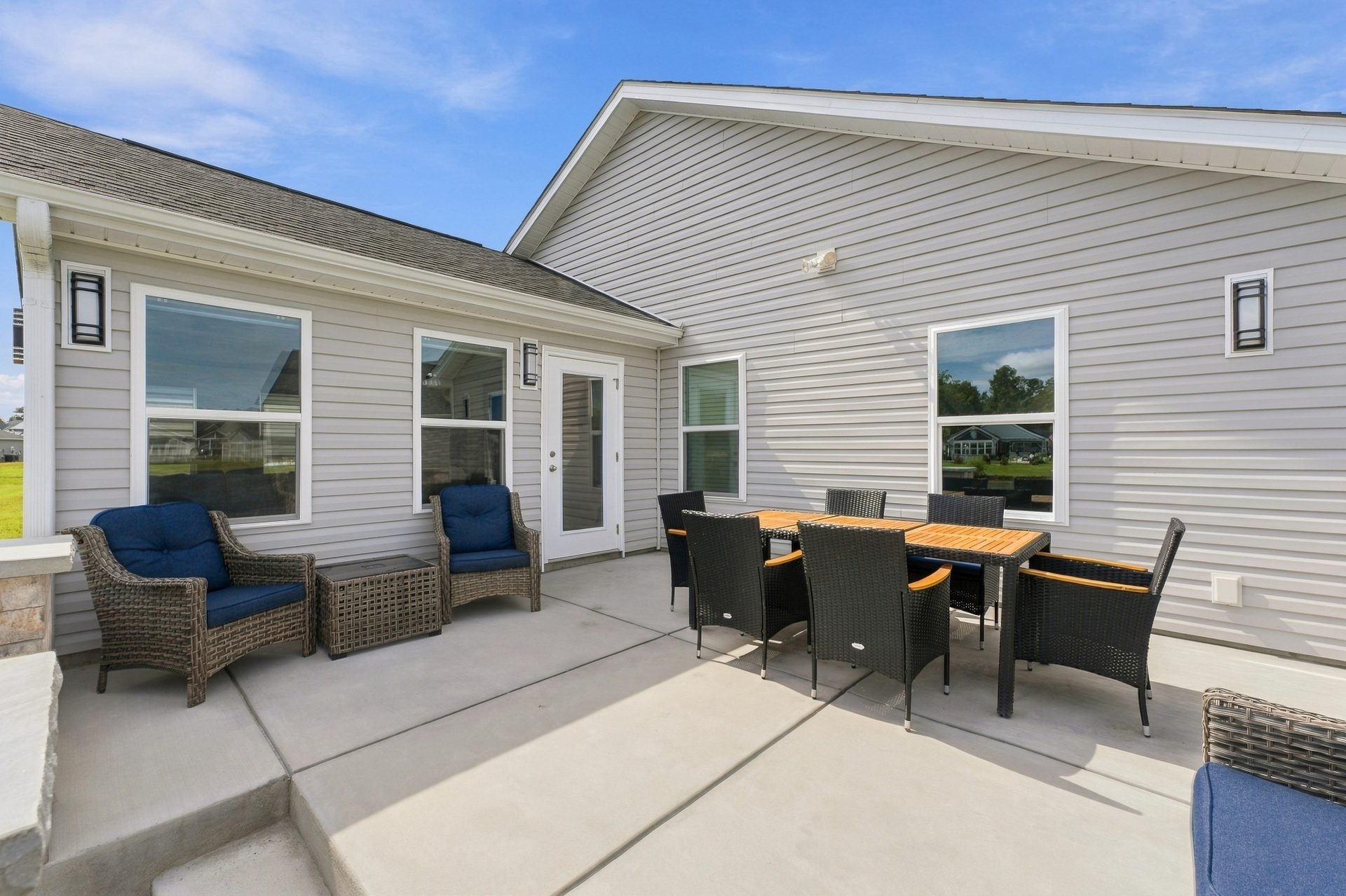 Concrete patio with an outdoor dining table and lounge chairs beside the sunroom addition
