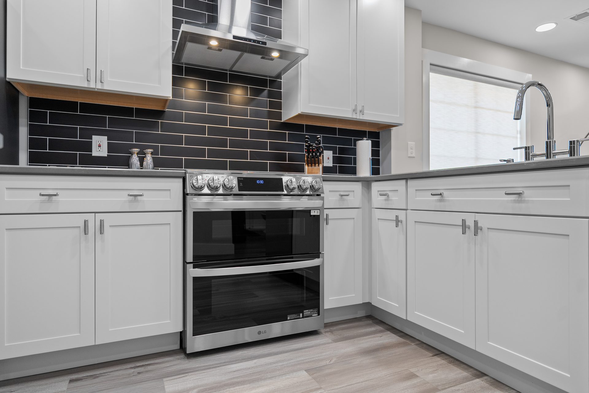 Kitchen range wall with slide-in double-oven range, stainless hood and full-height tile backsplash