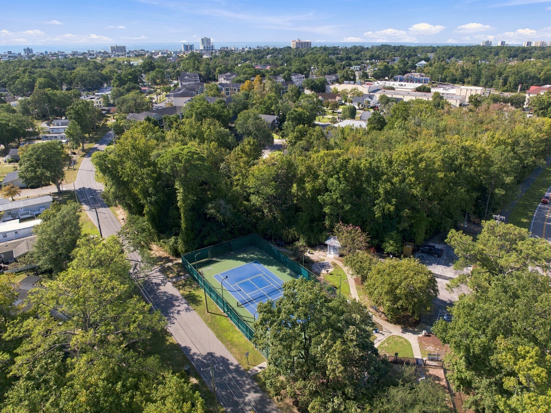 Aerial view over the North Myrtle Beach city park, with the tennis court and the restroom building among the trees and the coastline beyond