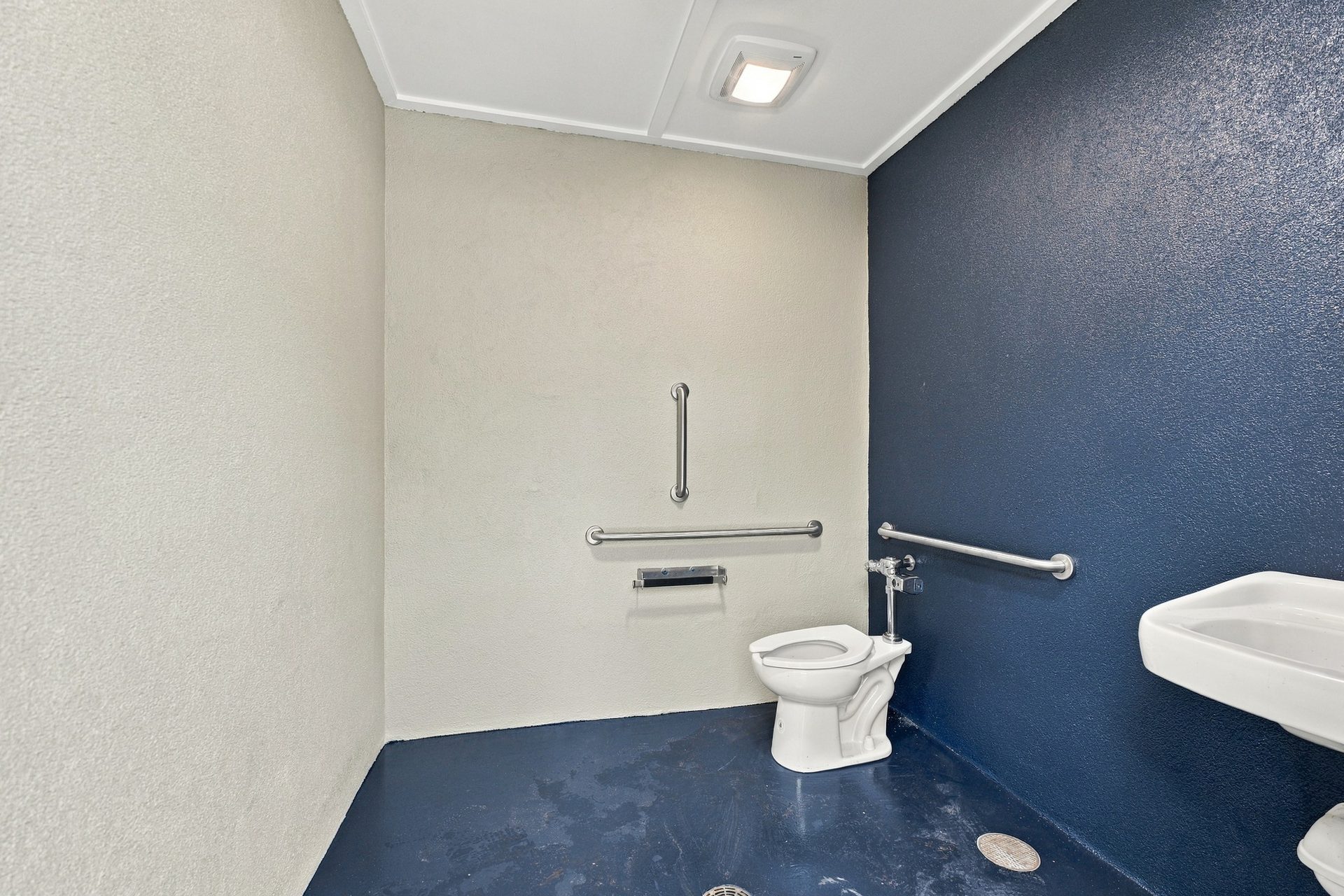 Interior of the accessible public restroom, with grab bars, a wall-hung sink and a sealed floor