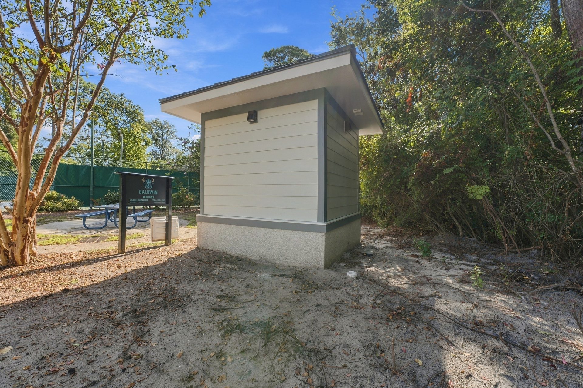 Rear elevation of the restroom building, with fiber-cement lap siding and a concrete base, beside the park tennis court